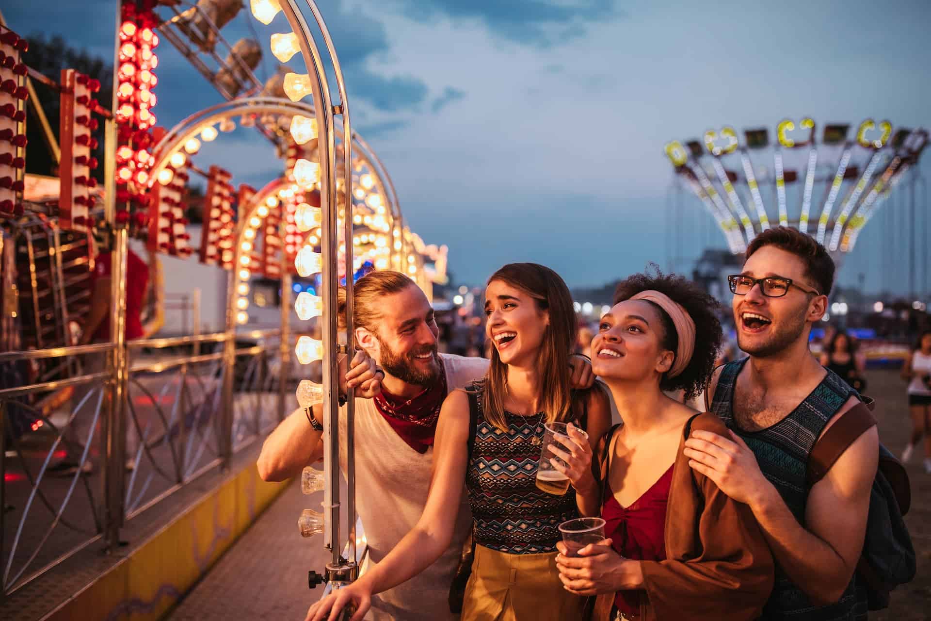 Four young adults laughing in front of the rides at dusk.